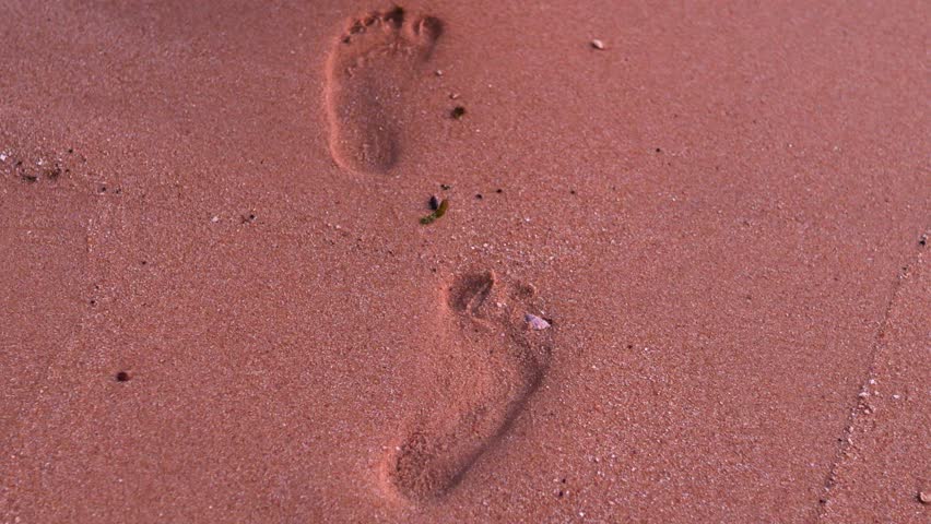 Footprints on pink sand at sunset.