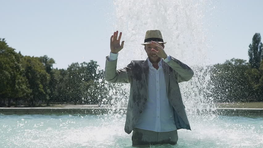 Happy Carefree Young Man In Vintage Fashion Style Having Fun in Water Fountain Outdoors in Summer Time