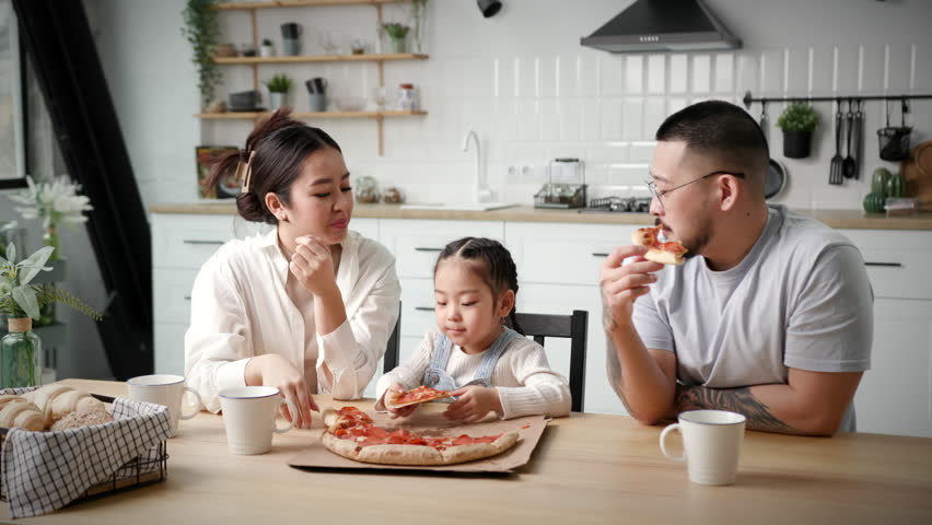 Happy Family Eating Pizza. Asian family with child eats pizza sitting at home. Parents chatting with kid during meal time. Royalty-Free Stock Footage #1102023597