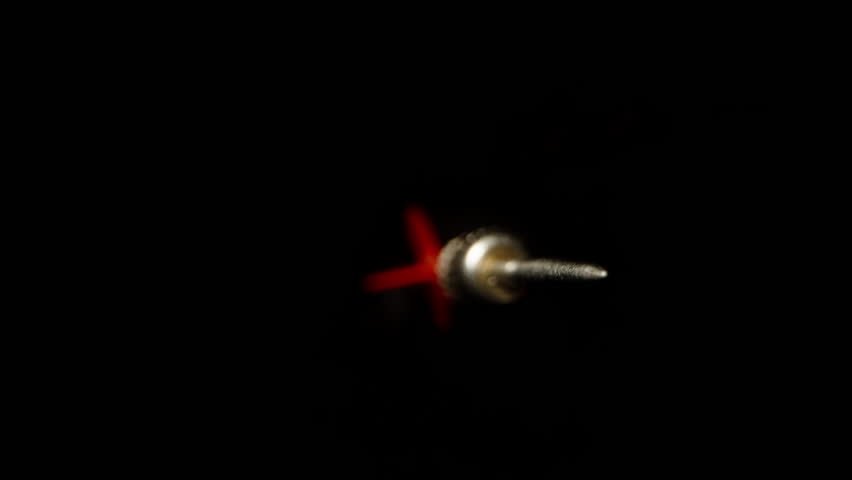 A red dart for playing darts rotates and flies on a black background to meet the camera, extremely close-up. Slow motion. Royalty-Free Stock Footage #1102027321