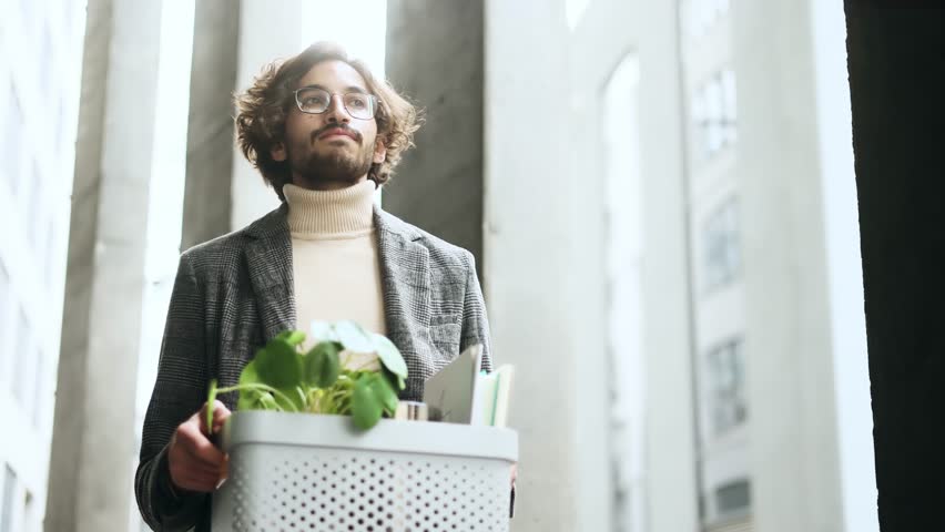 Portrait of fired sad young arabian businessman carries his box with personal belongings leaving the office centre Pensive muslim man with glasses thinking about future after unemployed  outdoors