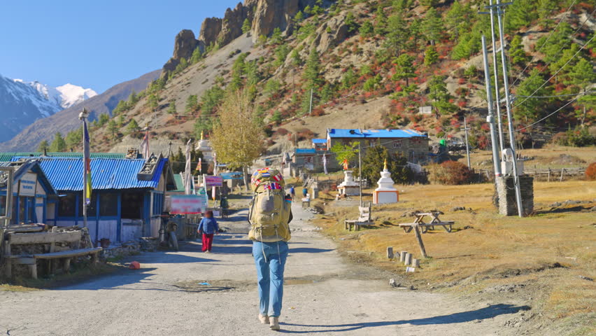 Rear view of lone trekker walking through small mountain village on the Annapurna Circuit Trek, Nepal