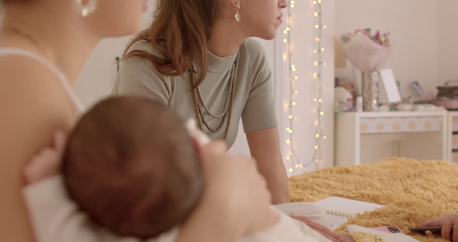 Woman sharing maternal experiences at meeting with friends. Mother with baby uses smartphone, smiling. Smartphone interaction during friendly gathering. Moments of laughter and smiles. Digital support