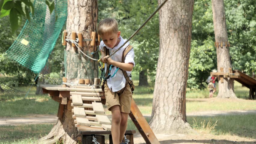 Little boy struggling walking on strung rope between trees in park. Active childhood, healthy lifestyle, kids playing outdoors, children in nature