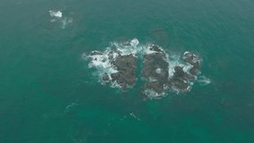 Waves crash against rocks in the ocean. A peaceful picture of nature. Aerial view of the rocks in water. The meeting place of the ocean and land. Slow motion 120 fps video