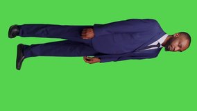 Vertical video: Side view of startup worker talking to people and waving in studio, wearing business suit over full body green screen. Young businessman having conversation on camera, calling someone - Powered by Shutterstock - Get 15% off with code: PIKWIZARD15