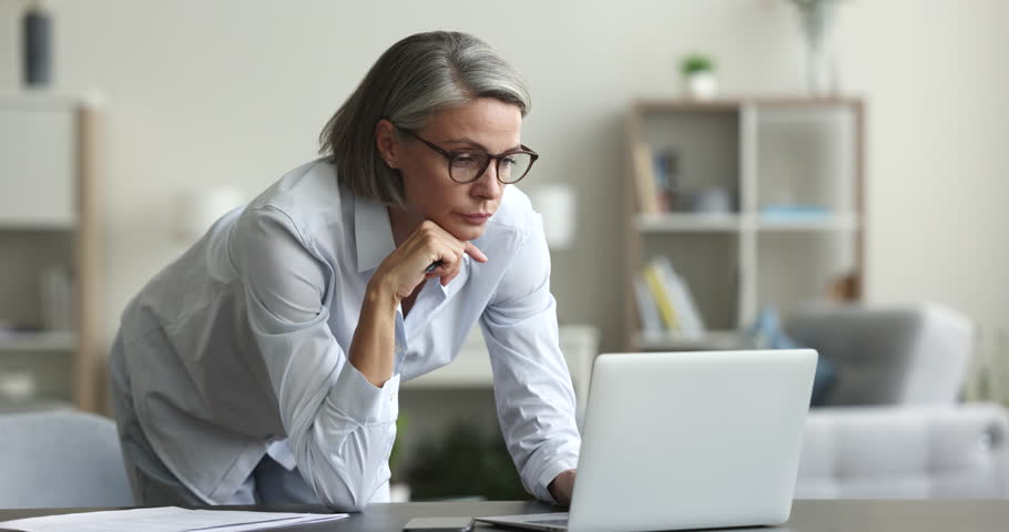 Pensive mature business woman, freelancer ponders working on laptop at homeoffice workplace, wear glasses looks at device screen, thinks over solution, search answer, busy in telework use modern tech Royalty-Free Stock Footage #1102040391
