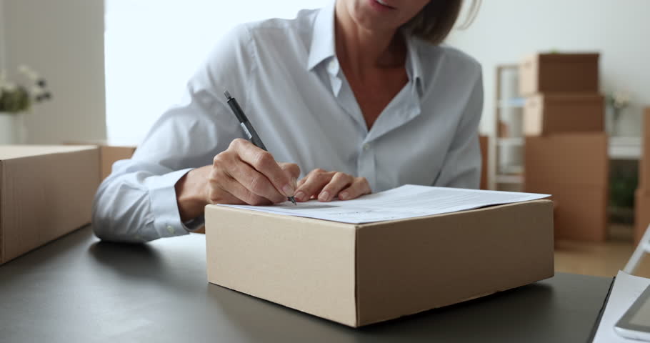 Close up woman, individual entrepreneur, small business owner prepares goods for sending to company customer, sit at desk filling address form on parcel. Shipment, delivery, merchandise, dropshipping Royalty-Free Stock Footage #1102040401