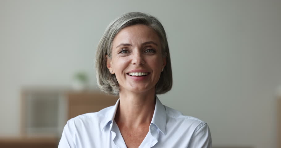 Head shot happy attractive businesslady staring at cam pose indoors. Portrait of mature woman having beautiful european appearance, positive mood, look at camera revealing wide toothy perfect smile | Shutterstock HD Video #1102040409