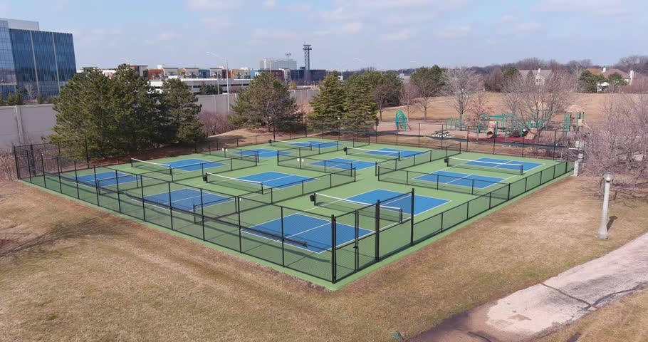 Aerial view of a new pickleball facility with blue and green courts in a suburban park in early spring.