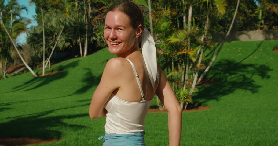 Happy carefree young woman spinning around herself on lawn in nature with outstreched arms. World smile day. Close-up slow-motion.