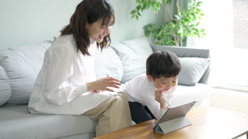 Parent and child sitting on the sofa and looking at the screen of the tablet PC Royalty-Free Stock Footage #1102044331