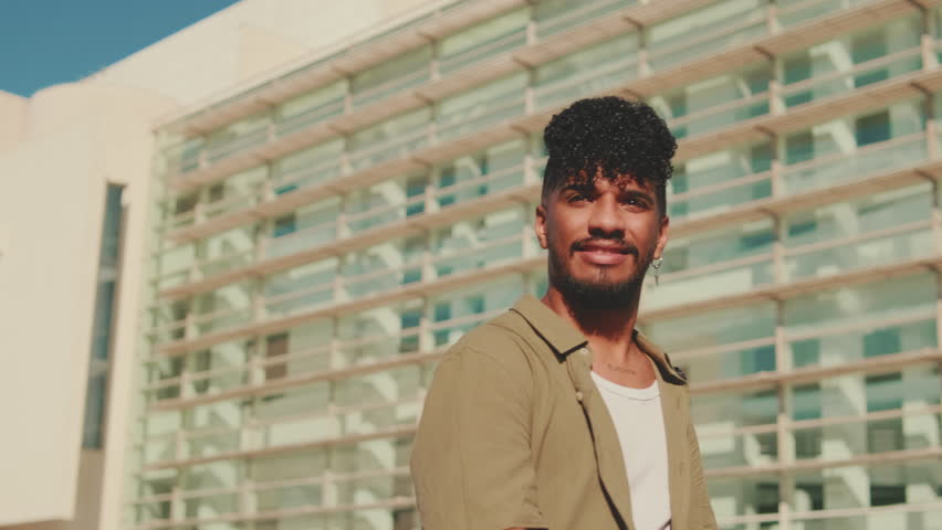 Young male student dressed in an olive-colored shirt walks from outside next to the university