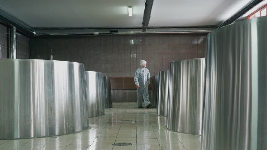 A brewery employee controls the process of brewing beer in a huge steel tanks in brewery factory