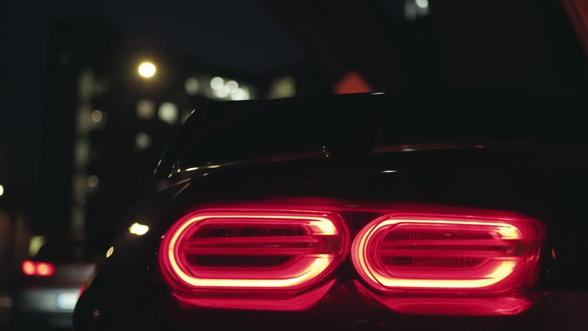 Black sports car tail light glowing in the dark of a night city