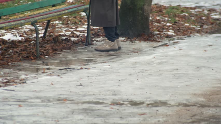 Elderly woman grandmother with a stick walks along the slippery sidewalk of a winter city