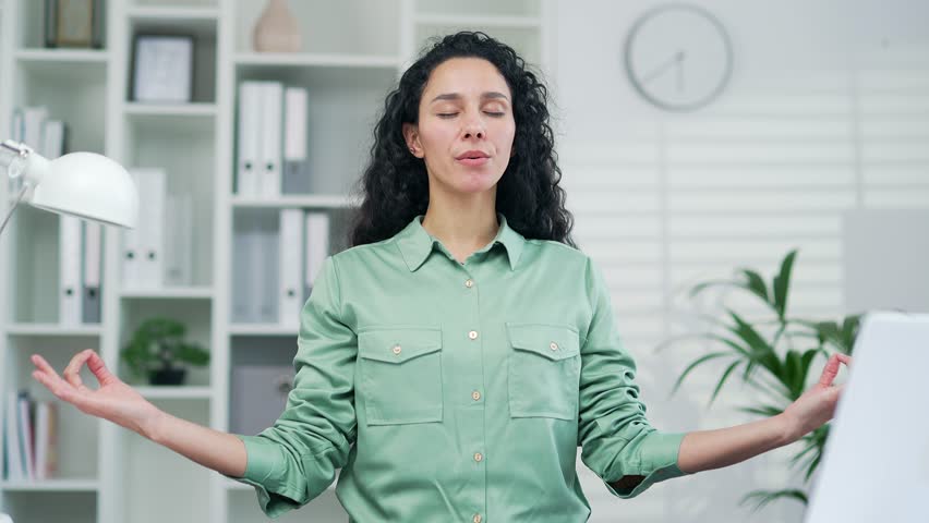 Calm employee worker practices yoga at workplace in the office Happy woman freelancer employee meditating relaxes in the office Serene carefree female sitting at a computer desk rest and ralax indoor