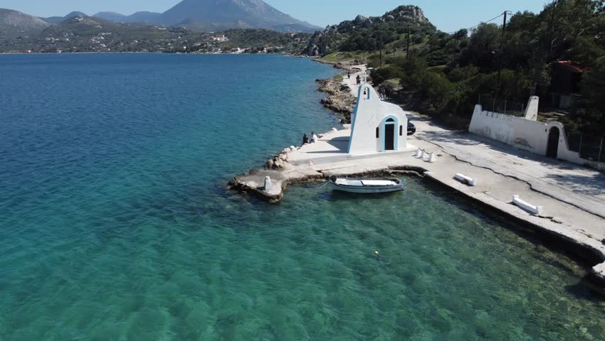 Aerial shot over a white little church and a small fishing boat in Lake Vouliagmeni, Loutraki Greece | 4K