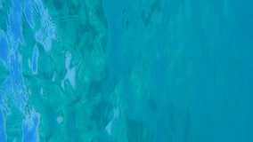 Vertical video, Underwater shot, surface of blue water with sun rays. Natural background with sun glints on surface of blue water. Texture of blue water surface
