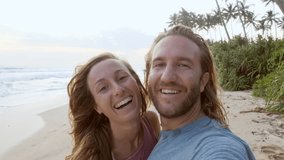 SLOW MOTION: beautiful couple taking selfie on beach at sunset enjoying tropical vacations and sharing online with friends video chatting waving hello on screen. Two people taking selfie video 