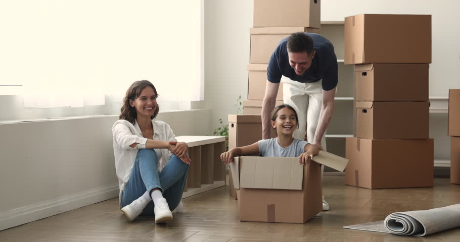 Laughing preteen 10s daughter give high five, enjoy playtime with parents seated inside cardboard box, celebrate relocation day. New home, bank loan for young family, life changes, housing improvement Royalty-Free Stock Footage #1102066325