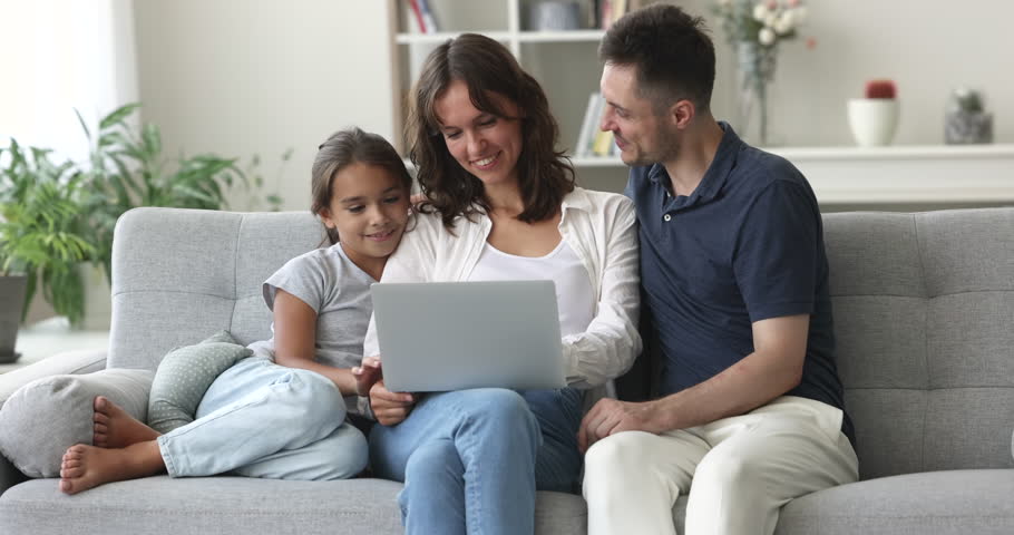 Happy Hispanic couple and little cute daughter resting together on couch watch funny videos, movie on-line, spend pastime on internet use laptop. Family leisure at home with modern wireless technology Royalty-Free Stock Footage #1102066355