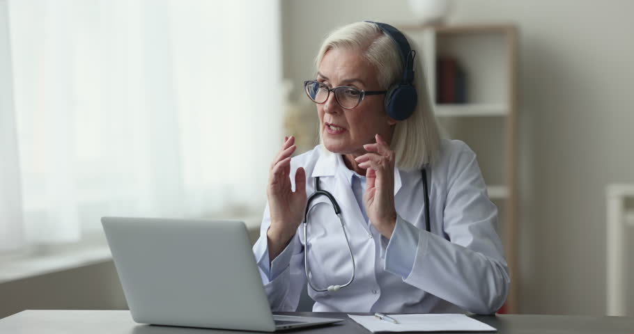 Mature doctor, female GP specialist provide professional helps remotely use video call on laptop, smile, give advice to clinic patient, explain diagnosis or treatment. Tech, medicine, e-health apps Royalty-Free Stock Footage #1102066371