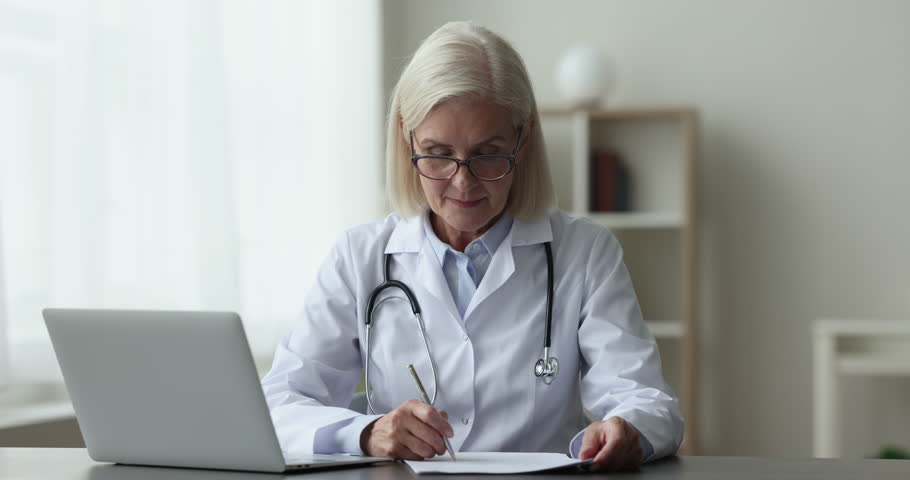 Ages confident professional medical worker, working sit at desk, writes notes, filling patient card, prepare report smile staring at camera, at workplace, Profession, reliable GP specialist portrait Royalty-Free Stock Footage #1102066375