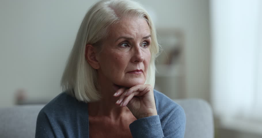 Close up sad, unhappy senior female sits on couch, looks in distance, have psychological problem, feels depressed, goes through older age crisis, worry about health, suffer from anxiety, miss of past Royalty-Free Stock Footage #1102066381