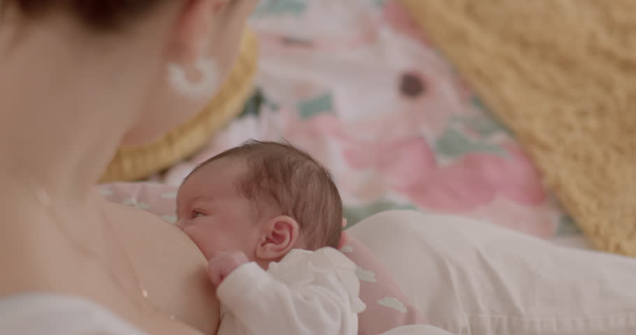 Unrecognizable young mother with sleeping newborn infant baby in her arms. Breastfeeding position and support babies for a good latch. Newborns may nurse for up to 20 minutes. Cozy lifestyle indoors. Royalty-Free Stock Footage #1102067305