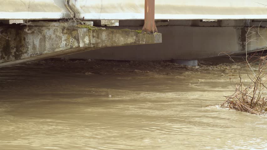 Floodwaters have risen all the way to top of bridge column. Thick big concrete pillars under water. An incredibly fast raging river. flow of a dangerous river. Slow motion