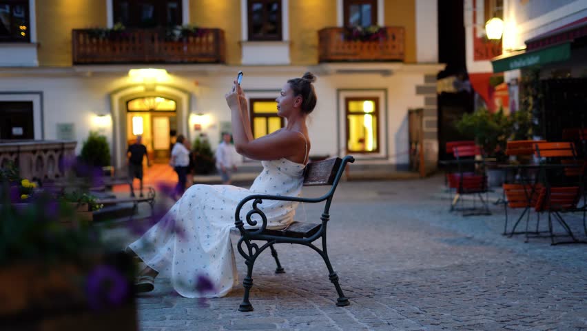 Woman sit in Hallstatt street at evening time and take a photo