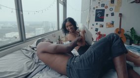 Young excited couple having fun and playing on bed in apartment, boyfriend tickling girlfriend, she laughing and fighting him with pillow. Handheld zoom shot - Powered by Shutterstock - Get 15% off with code: PIKWIZARD15