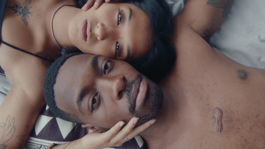 Overhead shot of young loving couple lying down head to head together on bed, gently touching each other, posing on camera