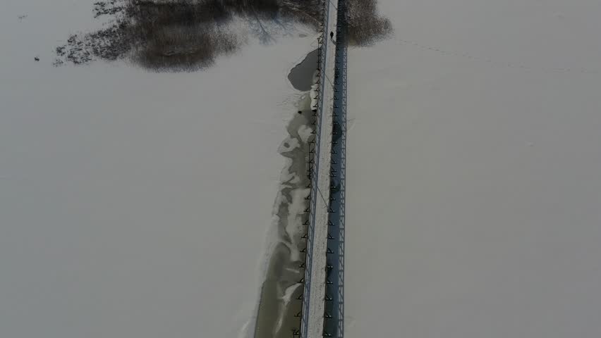 Long wooden winter bridge on snowy lake ice, aerial view

