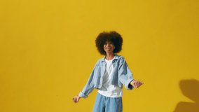 Playful happy young African American woman wear stylish denim clothes dancing and jumping funky black teen fashion girl on summer yellow background, horizontal banner header website design, copy space