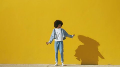 Playful happy young African American woman wear stylish blue denim clothes dancing and jumping funky black teen fashion girl on summer yellow background with copy space. Steady shot, full body – Video có sẵn