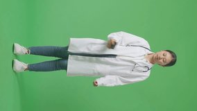 Full Body Of Asian Woman Doctor With Stethoscope Waving Hand And Having A Video Call On Smartphone While Standing On Green Screen Background In The Hospital
