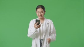 Asian Woman Doctor Waving Hand And Having A Video Call On Smartphone While Standing On Green Screen Background In The Hospital
