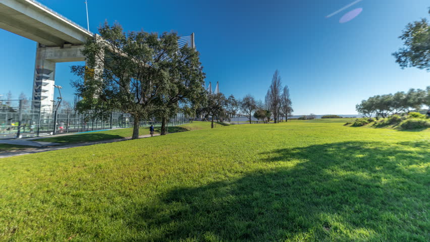 The Vasco da Gama Bridge timelapse hyperlapse viewed from green lawn with trees. Cable-stayed longest bridge flanked by viaducts and rangeviews that spans Tagus River in Park Nations. Lisbon, Portugal