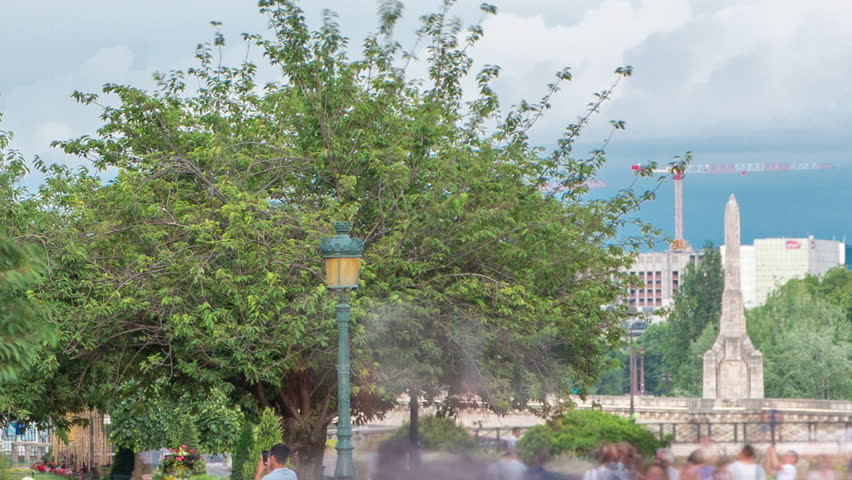 Notre Dame de Paris Garden on Cite Island timelapse, Paris, France. People walking in the park with green trees and flowers. Cloudy sky at summer day