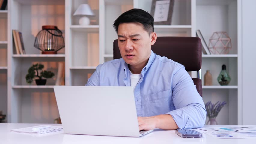 Exhausted Asian male manager sitting at desk in office, feeling overworked, bored with online project on the computer. Businessman is so tired trying to regain his energy. Needs rest to avoid burnout. Royalty-Free Stock Footage #1102089679