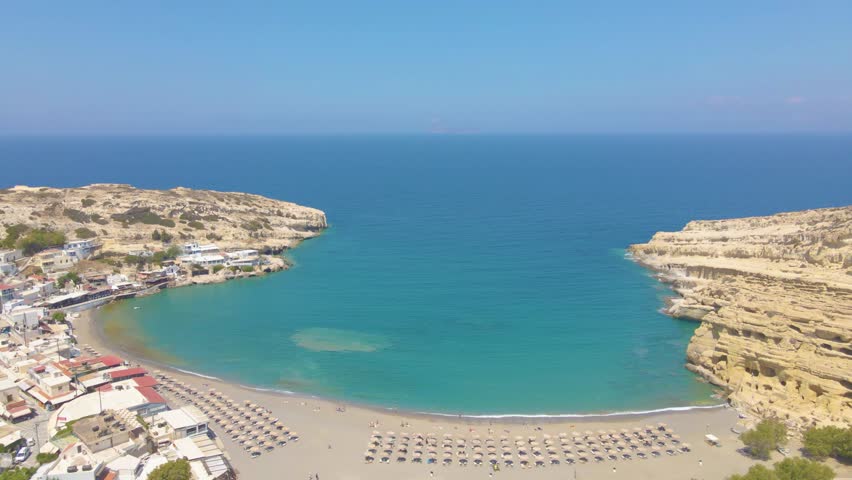 Aerial drone view of famous Matala beach in Crete island, Greece - with caves of hippies lived there in the 70’s