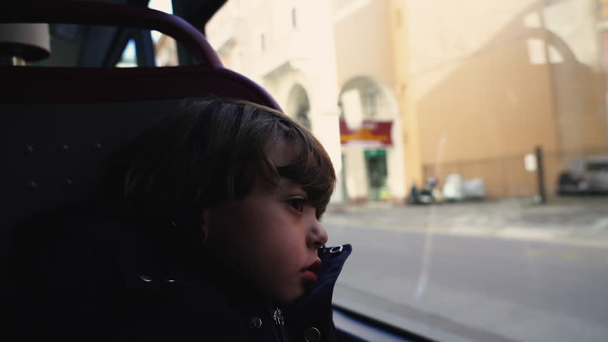 One contemplative little boy inside bus transportation. Child leaning on glass window looking at city with sad depressed emotion