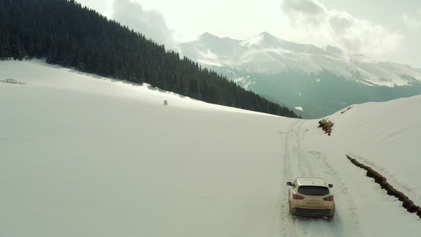 Tracking from behind a white car drives through deep snow in the mountains