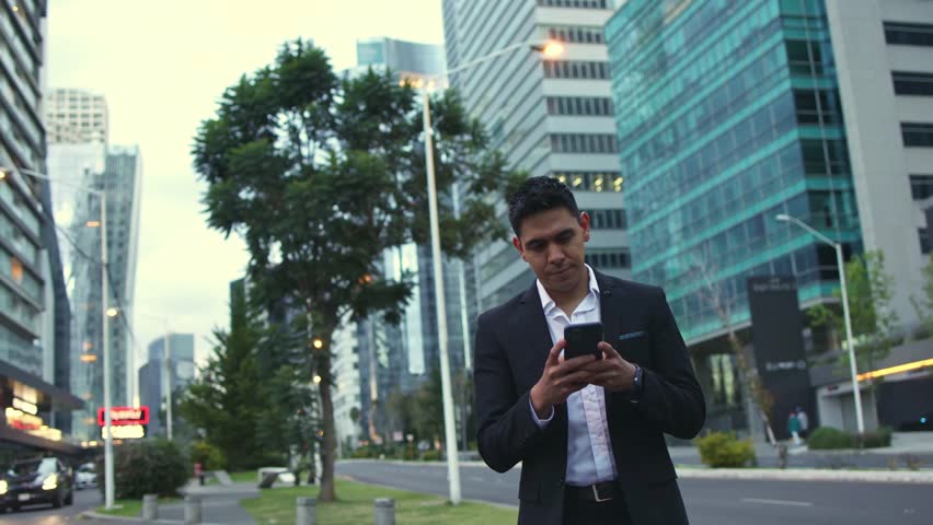 A portrait of a young smiling, happy, successful Mexican business man, executive walking outside down the street using mobile phone.  Royalty-Free Stock Footage #1102096107