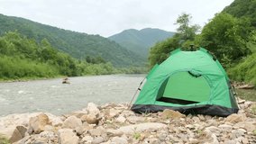 A beautiful view of the mountains, a mountain river, next to which there is a green tent. 