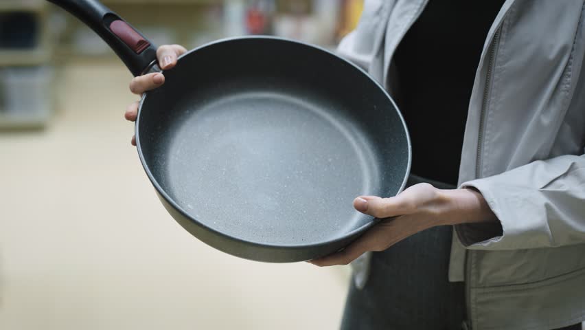 Hands of woman holding a new pan, choosing black teflon frying pan, customer deciding to buy non-stick frying pan for cooking food in her kitchen Royalty-Free Stock Footage #1102097729
