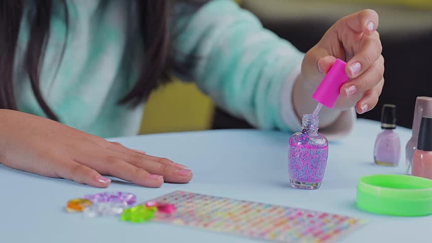 Unrecognizable teenager paints her nails with colored varnishes, on the table, at home