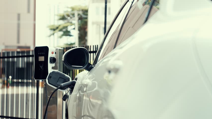 Progressive businesswoman unplug charger plug from charging station to his electric car before driving around city center. Eco friendly rechargeable car powered by sustainable and clean energy.
